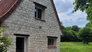 A stone house with a tiled roof, a wooden table and chairs outside, and a grassy field in the background. - Maison 1810, the charm of old stones. (Fosseux)