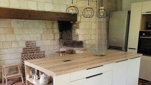 A kitchen with a brick wall, wooden beams, a built-in island with drawers, a hanging light fixture, and a modern refrigerator. - Maison 1810, the charm of old stones. (Fosseux)