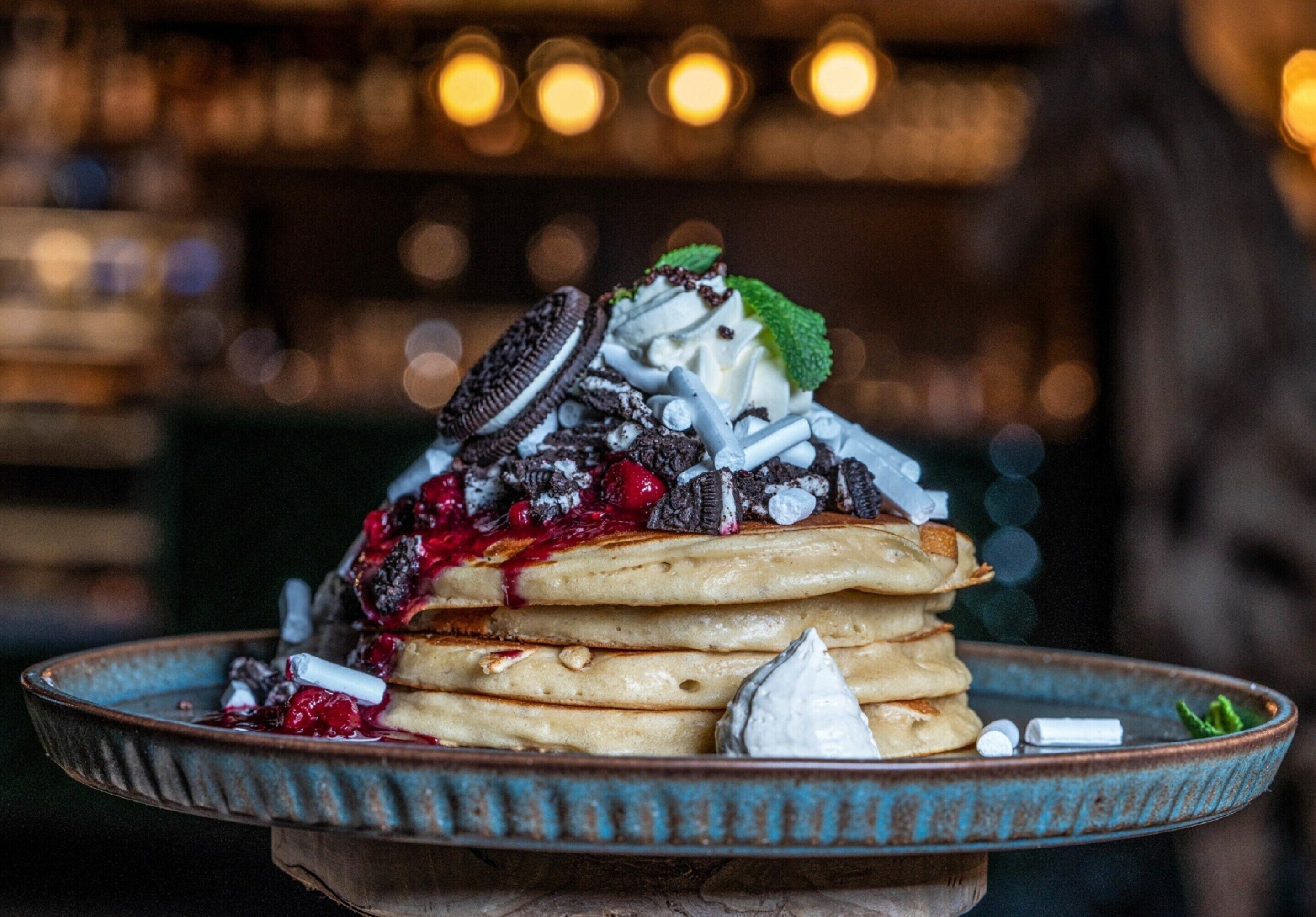 Un postre con varias capas, que incluye tortitas, crema batida y diferentes ingredientes como frutos rojos y galletas.