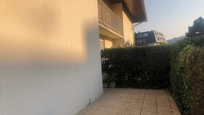 Eine gepflasterte Terrasse mit einer Holzbank, umgeben von weißen Mauern und einem Heckenstreifen.