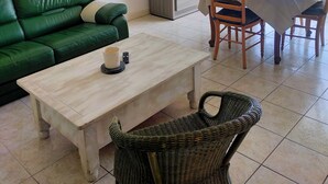 Ein Wohnbereich mit grünem Sofa, einem Holztisch, einem Korbstuhl, einem Esstisch mit Stühlen und einem Schrank mit Glastüren.
