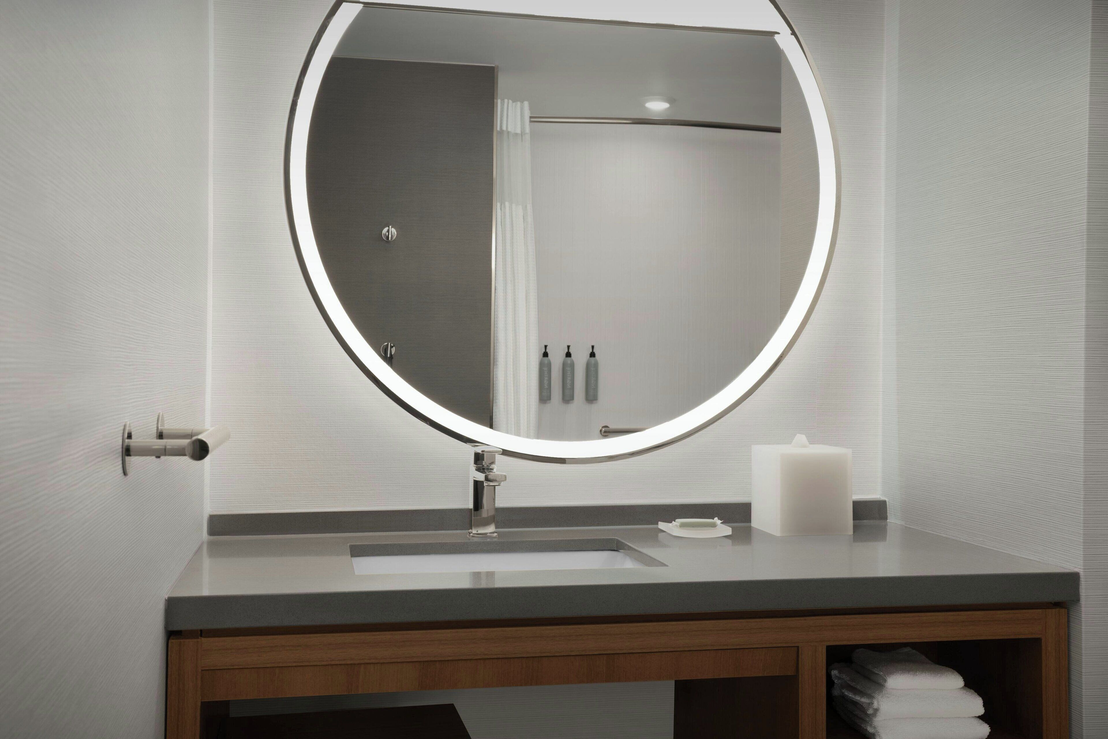 Un baño moderno con un espejo redondo, un lavabo y un tocador de madera.