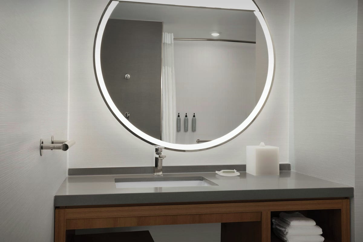 Un baño moderno con un espejo redondo, un lavabo y un tocador de madera.