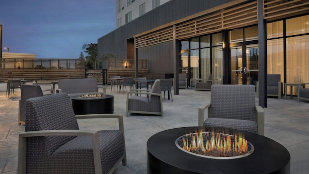 An outdoor seating area with fire pits and modern furniture, a building with large windows, and a wooden deck.