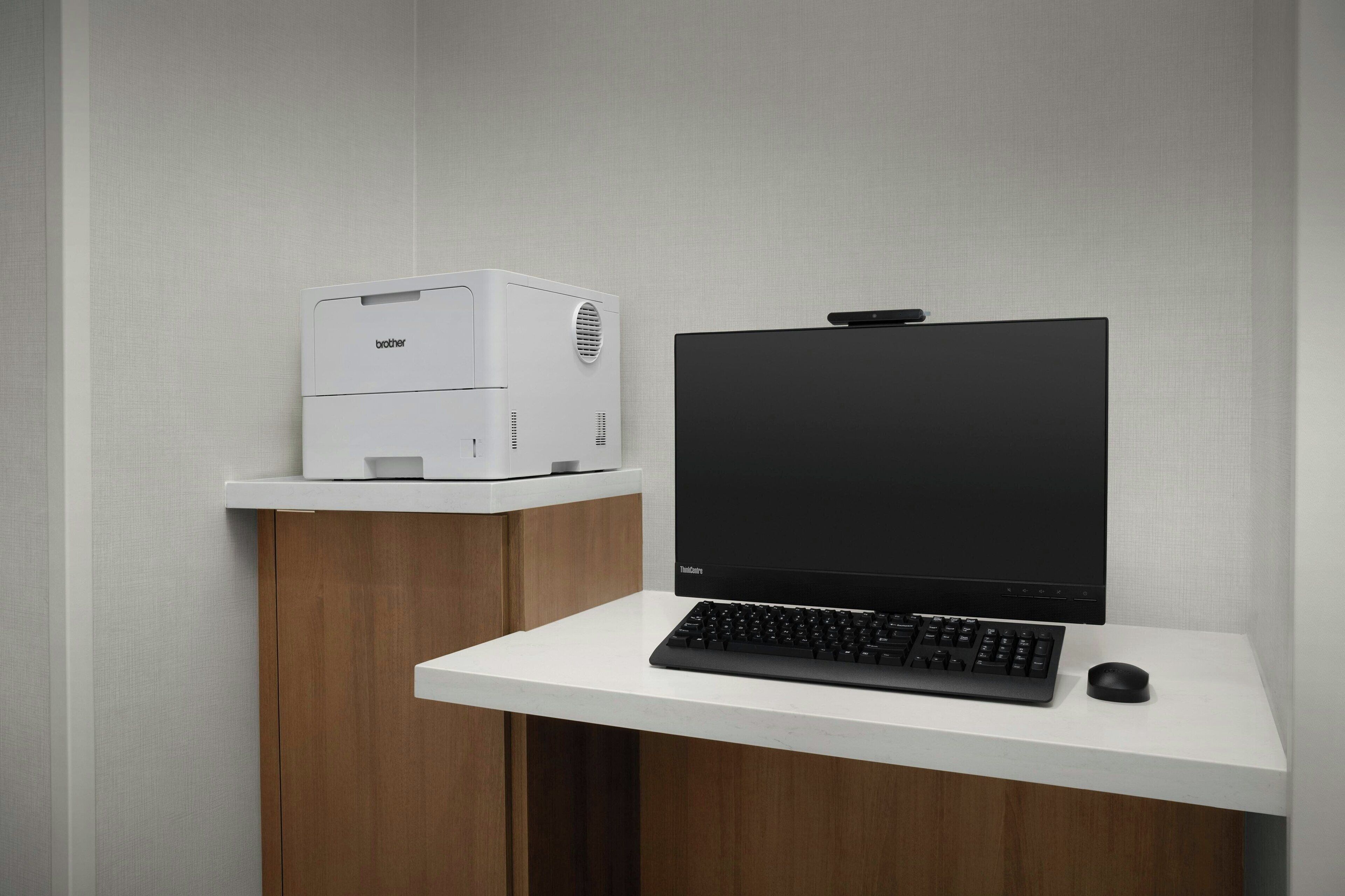 A modern office setup with a desktop computer, a printer, and a keyboard on a white desk against a wooden cabinet.