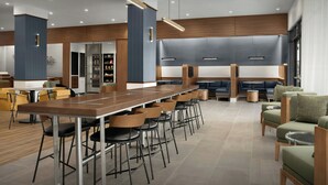 A modern lounge area with a long communal table, multiple bar stools, and seating arrangements.