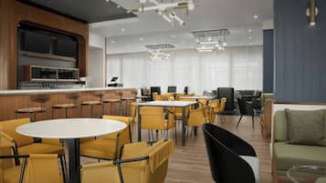 Eine moderne Hotelhalle mit runden Tischen, gelben Stühlen, einer Bar und einer Sitzecke mit Sofas.