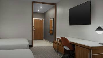 A hotel room with two beds, a desk, a chair, a flat-screen TV, a mirror, and a small dresser.