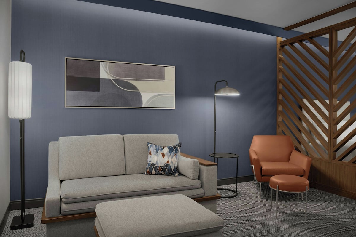 A modern living room with a grey sofa, an orange armchair, a patterned throw pillow, a floor lamp, and a geometric abstract painting on the wall.