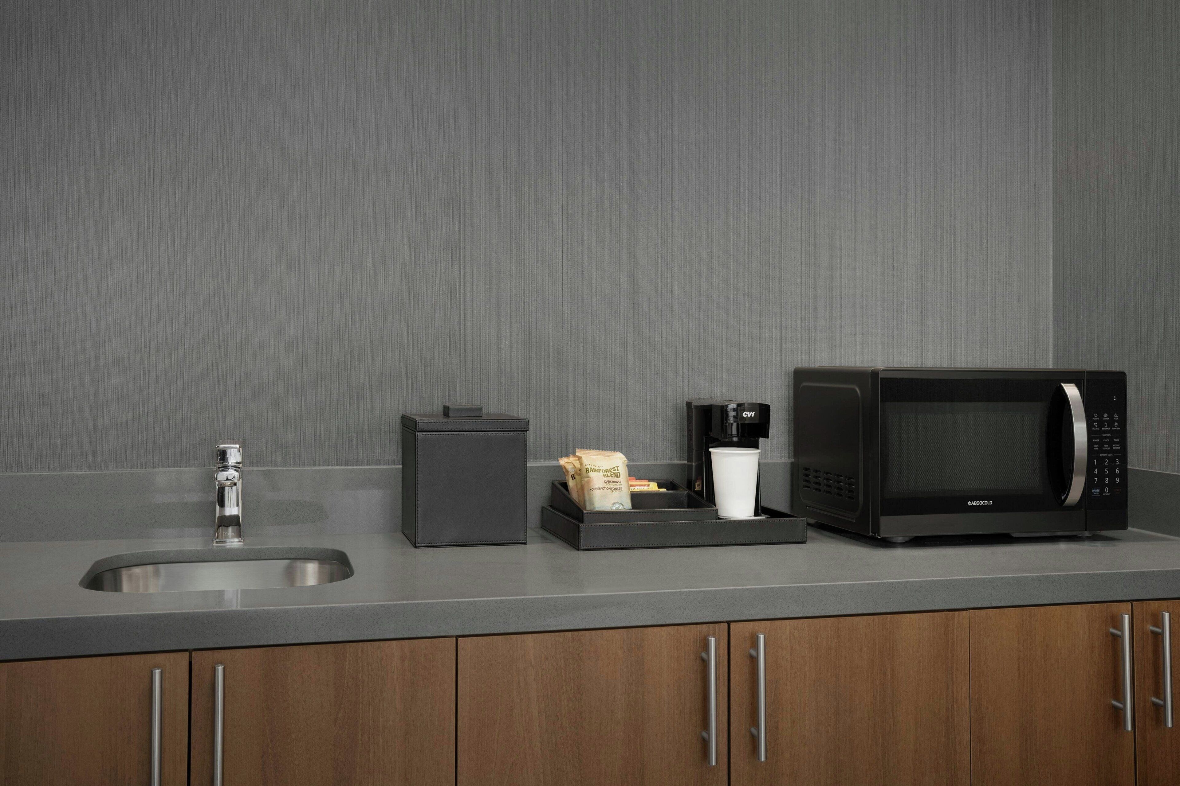 Una cocina con un lavaplatos de acero inoxidable, un microondas negro, una cafetera y un mueble pequeño.