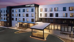 A Courtyard by Marriott hotel with a modern design, featuring multiple floors, large windows, and a covered outdoor seating area.