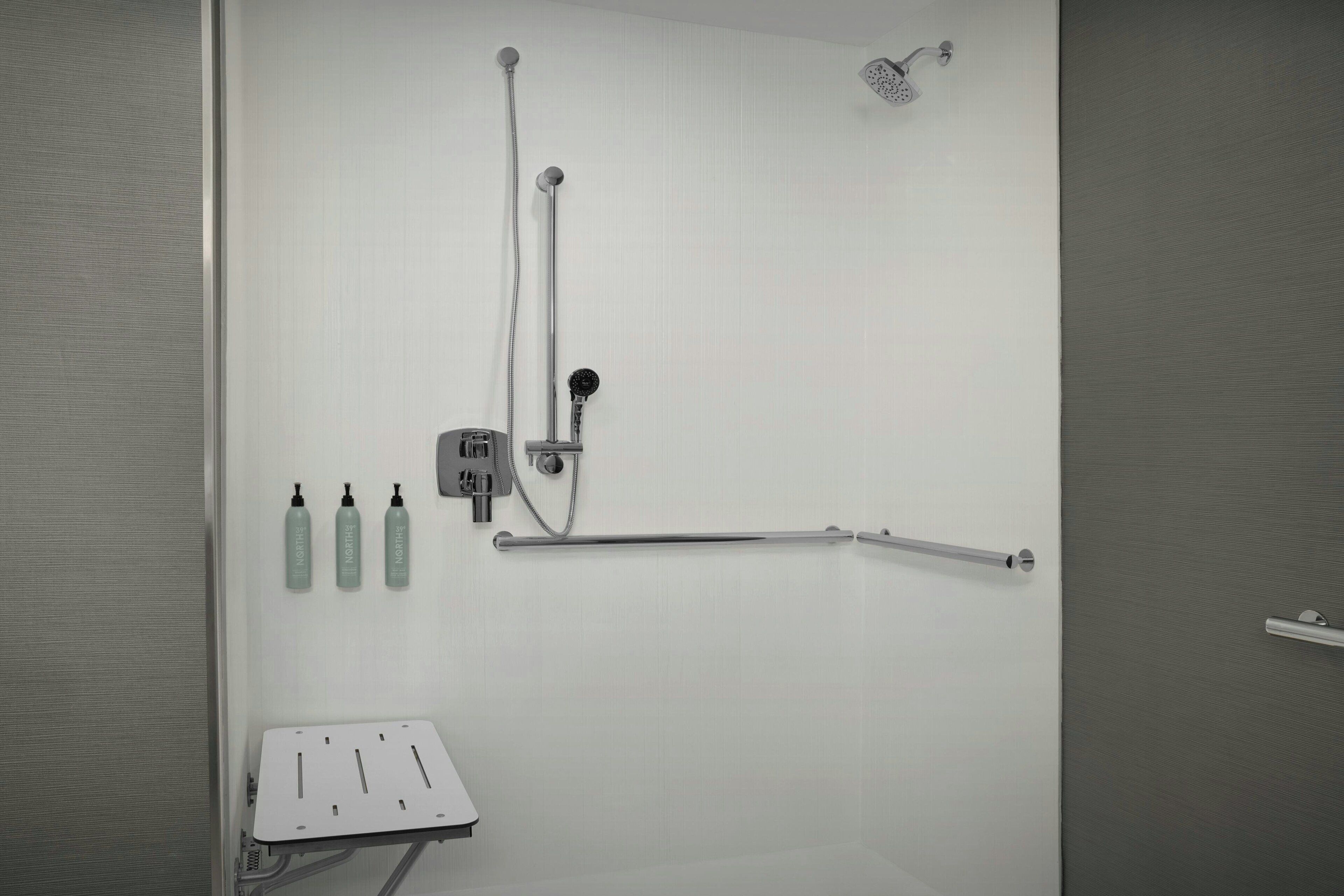 A shower area with a handheld showerhead, a wall-mounted faucet, and a handheld shower attachment. There are three bottles of shampoo and conditioner on the wall.