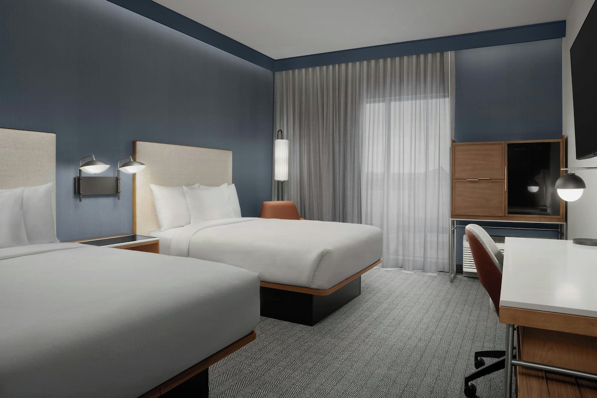 A hotel room with two beds, a desk, a chair, a TV, and a window with curtains.