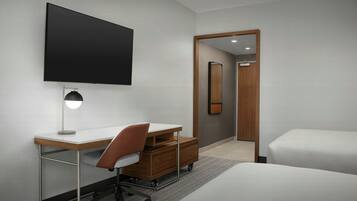 A modern hotel room with a flat-screen TV, a desk with a chair, a bed, and a large mirror.