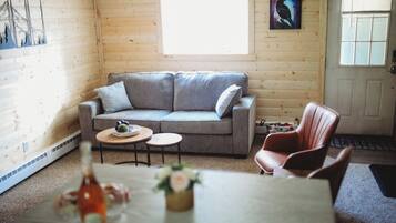 A cozy room with a grey sofa, two small round tables, a wooden floor, a door, and a window.