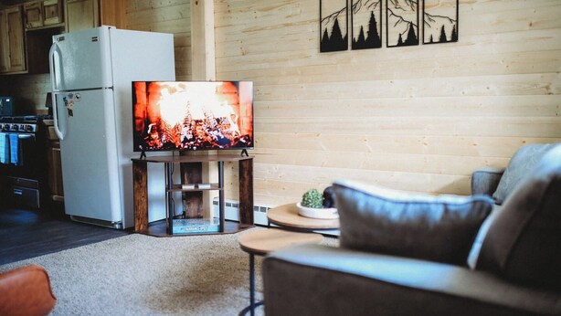 Un salon chaleureux avec un téléviseur posé sur un meuble, un canapé et un mur en bois orné de tableaux encadrés.