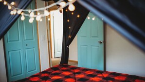 Une chambre avec une couvre-lit à carreaux rouges et noirs, des portes de couleur turquoise et des guirlandes lumineuses.