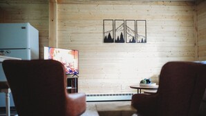 Une pièce chaleureuse aux murs en bois, dotée d’un téléviseur à écran plat, de deux fauteuils, d’une petite table et d’un élément décoratif mural.