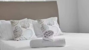 A neatly made bed with a rolled towel, white pillows with a shell pattern, and a plain headboard. - Heart of Calle 8 | Spacious 2/2 for Families (Miami)
