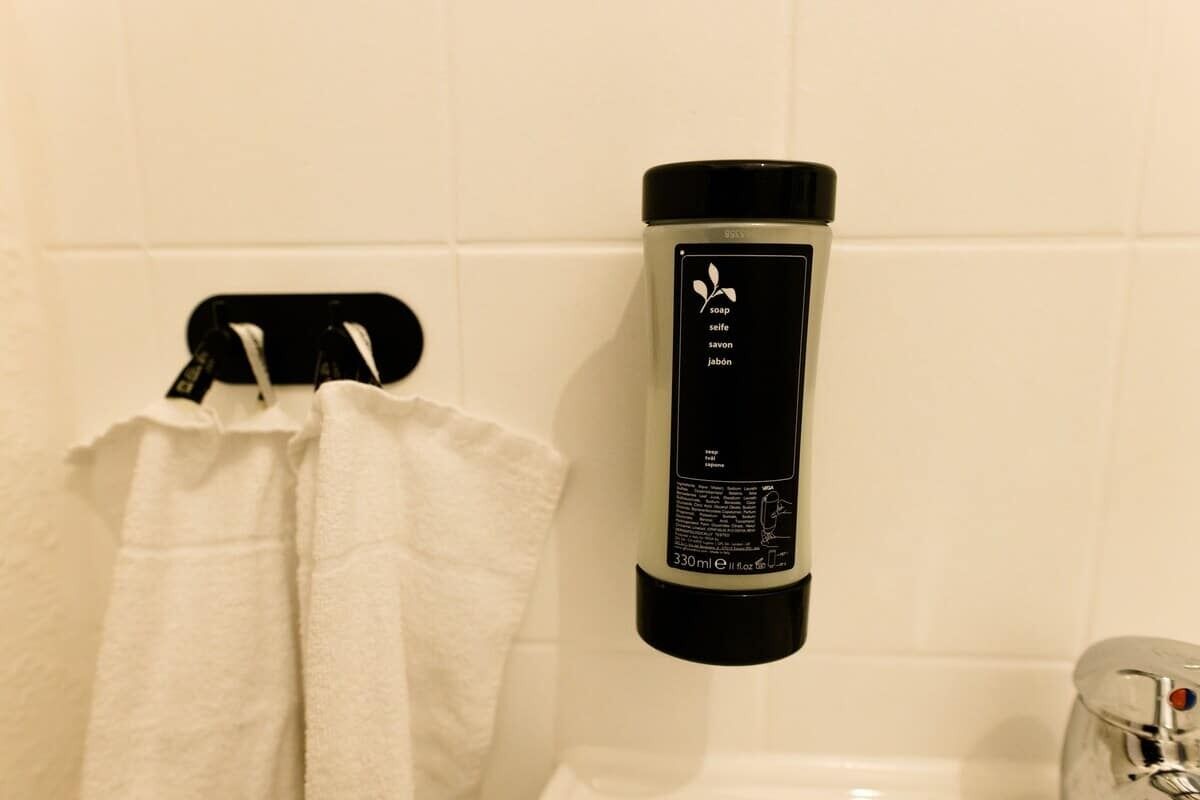 A bathroom with a white towel hanging on a rack, a black soap dispenser, and a white tiled wall.