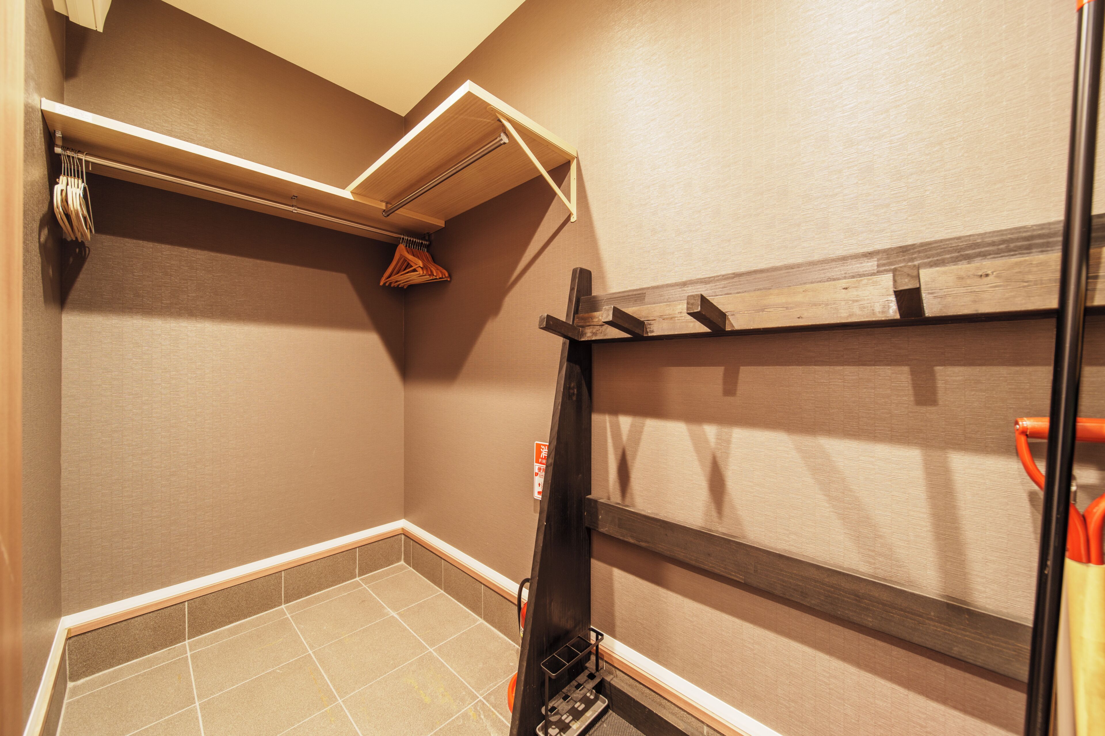 A bathroom with a tiled floor, a wooden shelf, and a hanging towel rack.