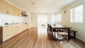 Una cucina moderna con mobili in legno, un'area pranzo con tavolo e sedie, e ampie finestre che lasciano entrare luce naturale.