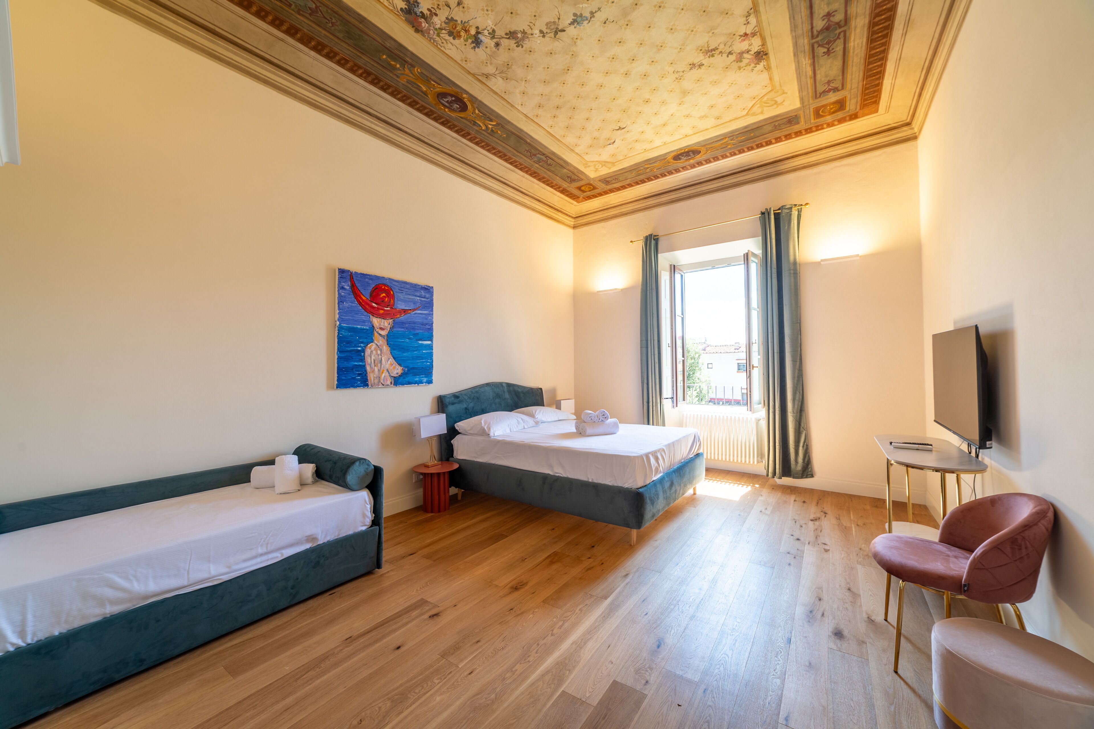 A hotel room with two beds, a desk, a chair, a painting, and a television.