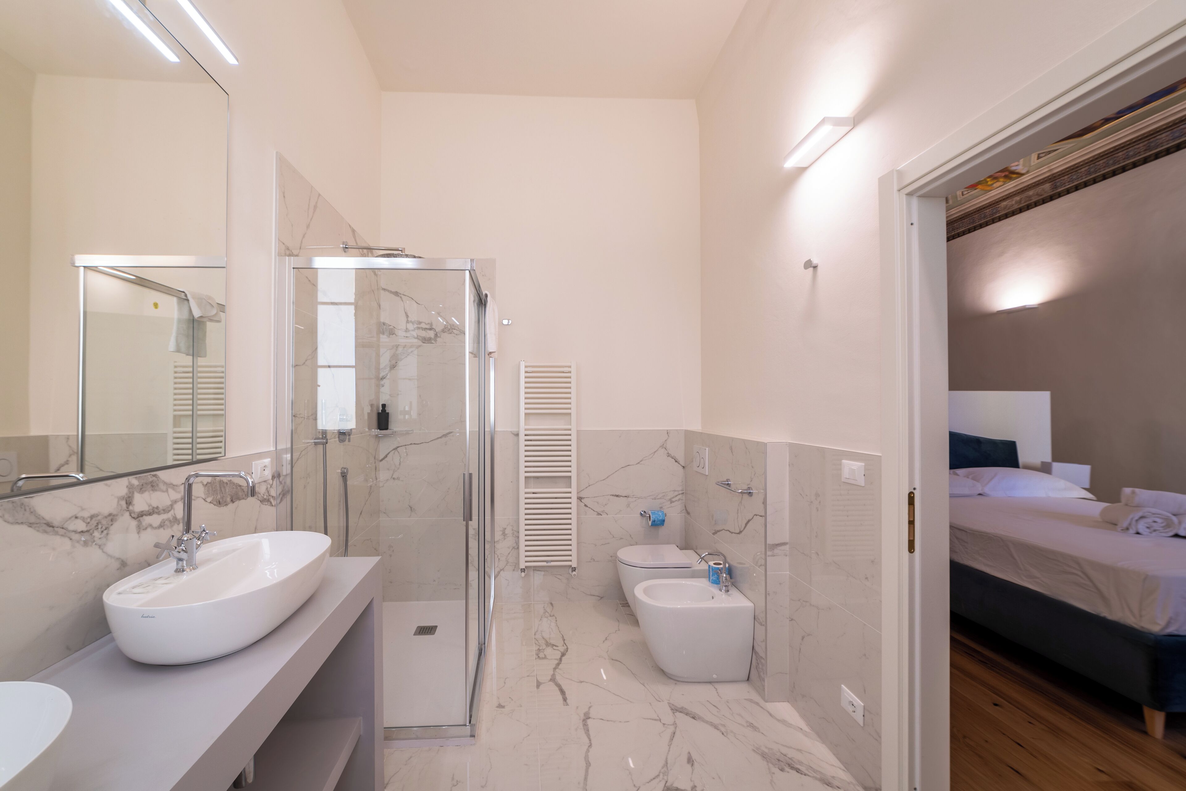 A modern bathroom with a large mirror, two sinks, a shower, and a bidet.