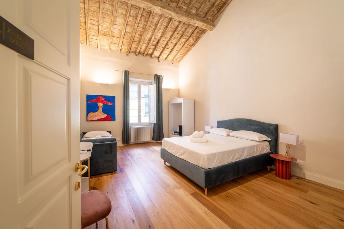 Une chambre à coucher comprenant un lit, une chaise, une petite table, un radiateur et une fenêtre avec des rideaux.