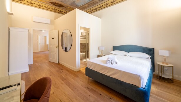 A bedroom with a large bed, a mirror, a chair, and a ceiling with decorative elements. - Palazzo Salviati Quaratesi (Florence)