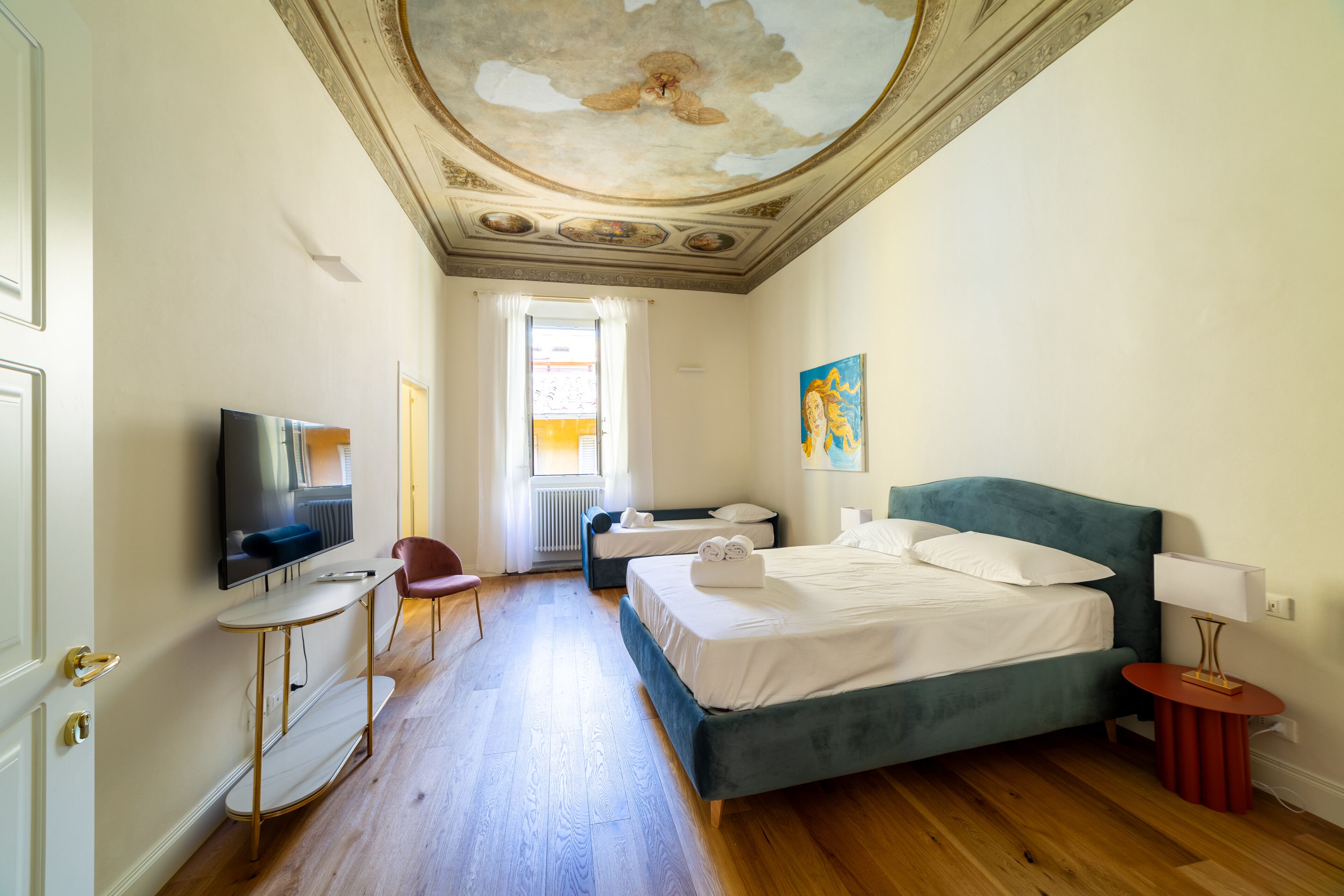 Ein Hotelzimmer mit einem großen Bett, einem Fernseher, einem kleinen Tisch, einem Sessel und einer Zierdecke.