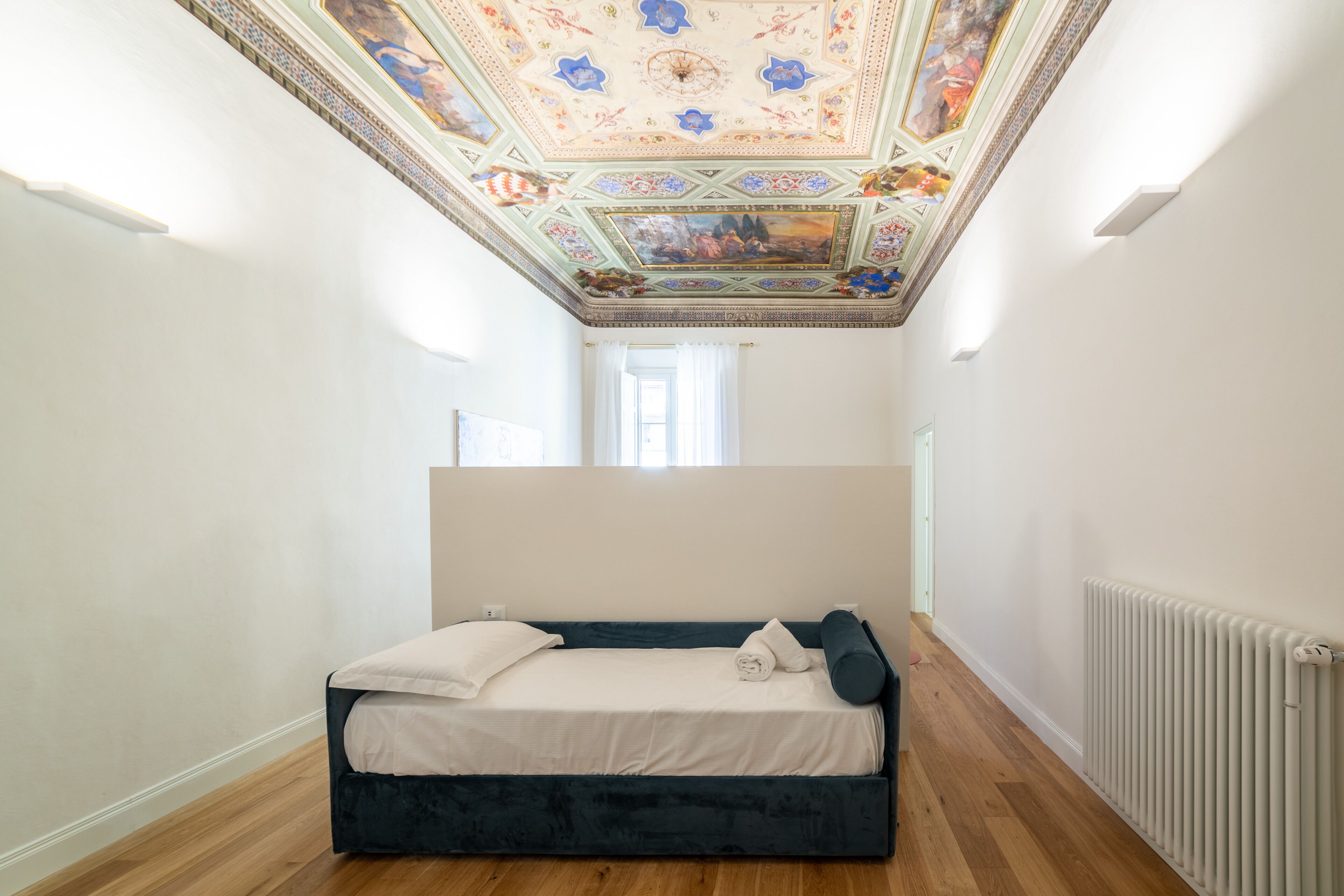 Ein Schlafzimmer mit einem Bett, einem Heizkörper und einer Decke mit aufwendigen Fresken.