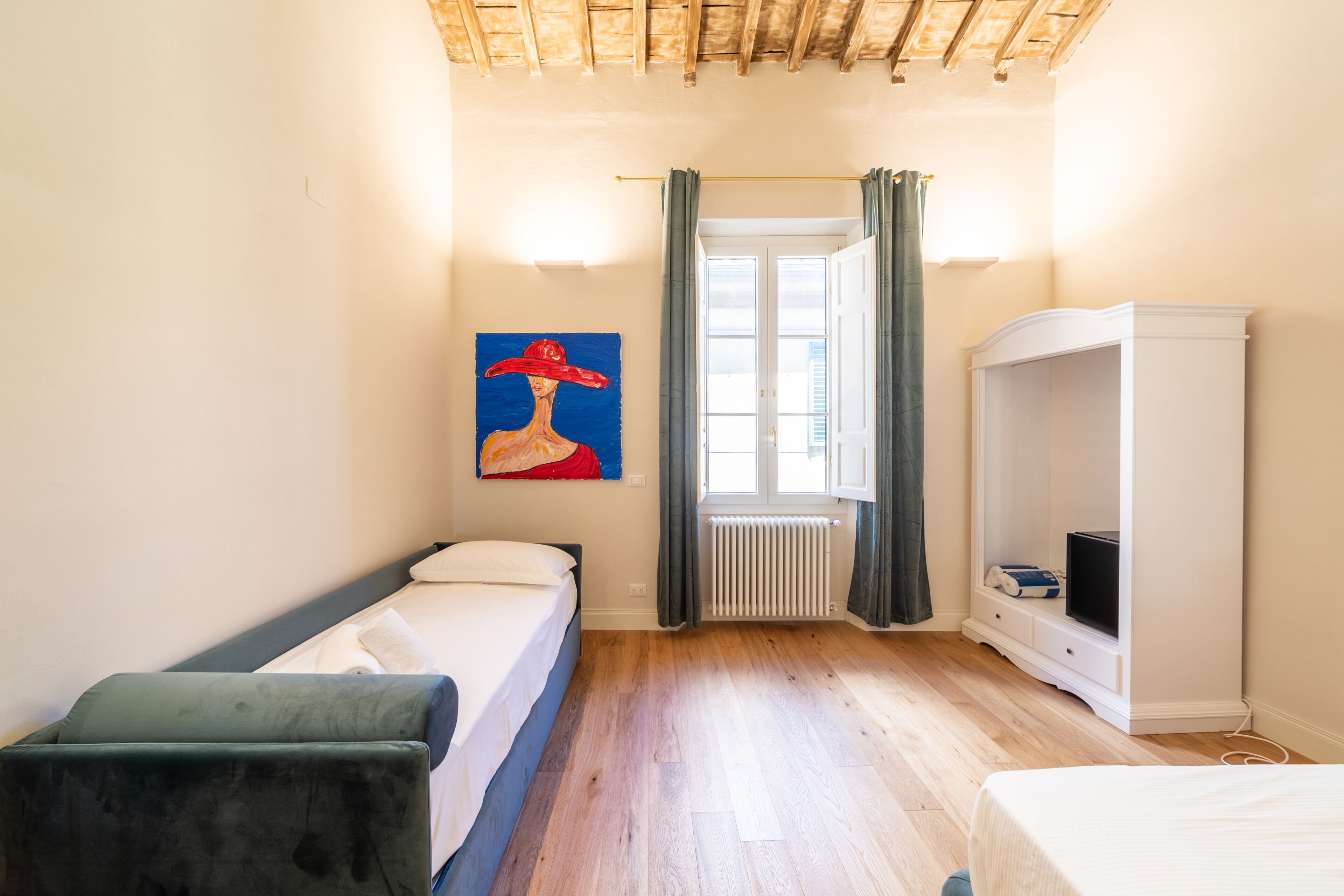 Un dormitorio con cama, armario, radiador y ventana con cortinas.