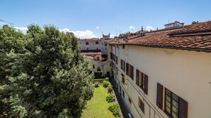 A narrow street with buildings on either side, a tree-lined courtyard, and a clear blue sky. - Palazzo Salviati Quaratesi (Florence)