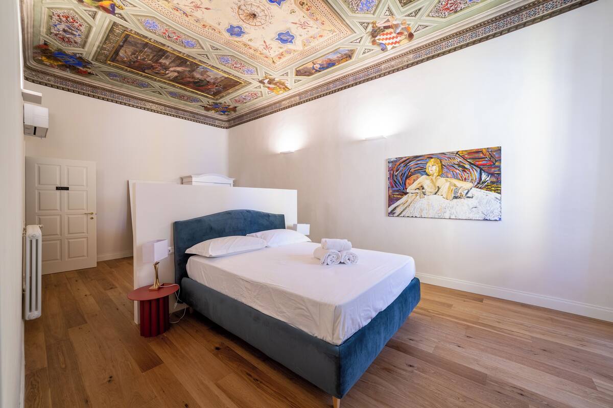 Une chambre avec un grand lit, un plafond orné de motifs décoratifs et un tableau accroché au mur.