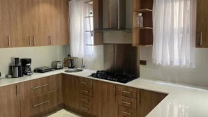 A modern kitchen with wooden cabinets, a gas stove, a coffee maker, and a toaster. - Roma Park 2 Bedroom Villa (Lusaka)