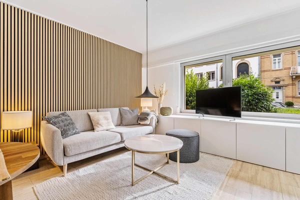 Cozy lounge space with elegant wood accents, a comfortable sofa, and a peaceful view toward the garden, perfect for unwinding after a day in Limpertsberg.