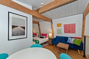 A room with a bed, a blue sofa, a round table, and a wall with framed pictures. - Summit View Treehouse By Destination Big Bear: Pet Friendly! Close to Bear Mtn! Walking Distance to Alpine Zoo! (Big Bear Lake)