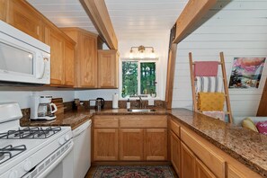 A kitchen with wooden cabinets, a stove, a microwave, and a coffee maker. - Summit View Treehouse By Destination Big Bear: Pet Friendly! Close to Bear Mtn! Walking Distance to Alpine Zoo! (Big Bear Lake)