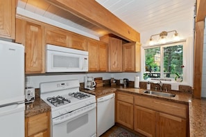 A kitchen with wooden cabinets, a gas stove, a microwave, and a sink. - Summit View Treehouse By Destination Big Bear: Pet Friendly! Close to Bear Mtn! Walking Distance to Alpine Zoo! (Big Bear Lake)