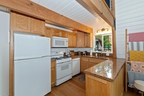 A compact kitchen with wooden cabinets, a white refrigerator, a microwave, a stove, and a dishwasher.