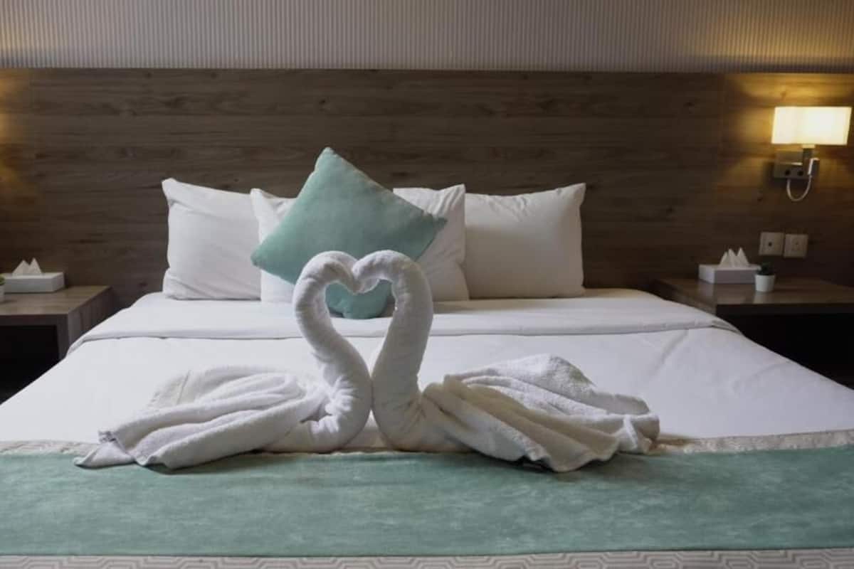 A hotel room with a bed, two nightstands, a wall-mounted lamp, and a decorative towel arrangement on the bed.