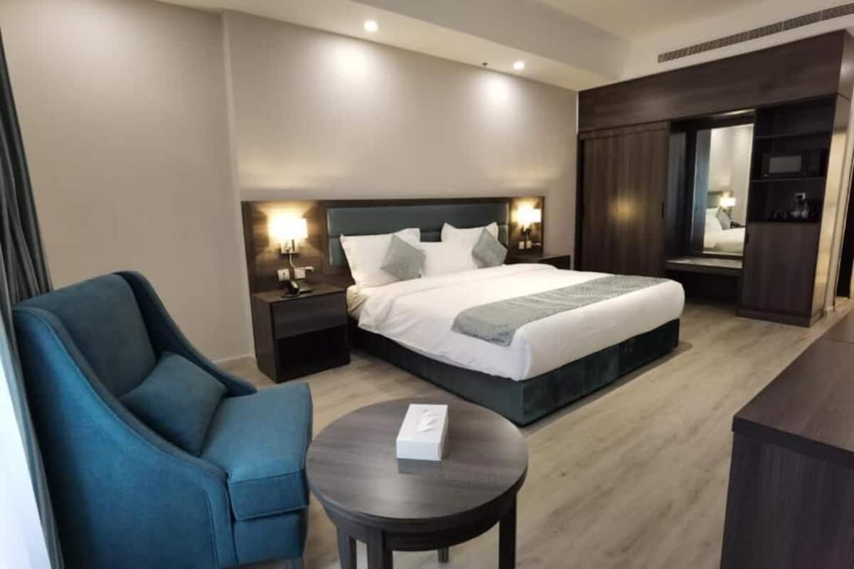 A hotel room with a bed, a blue armchair, a small round table, and a wardrobe.