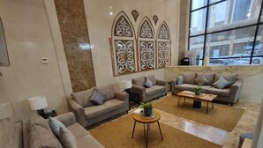 Amplia sala de estar con varios sofás y una mesa de centro, un panel decorativo en la pared y un ventanal que ofrece vistas al exterior.