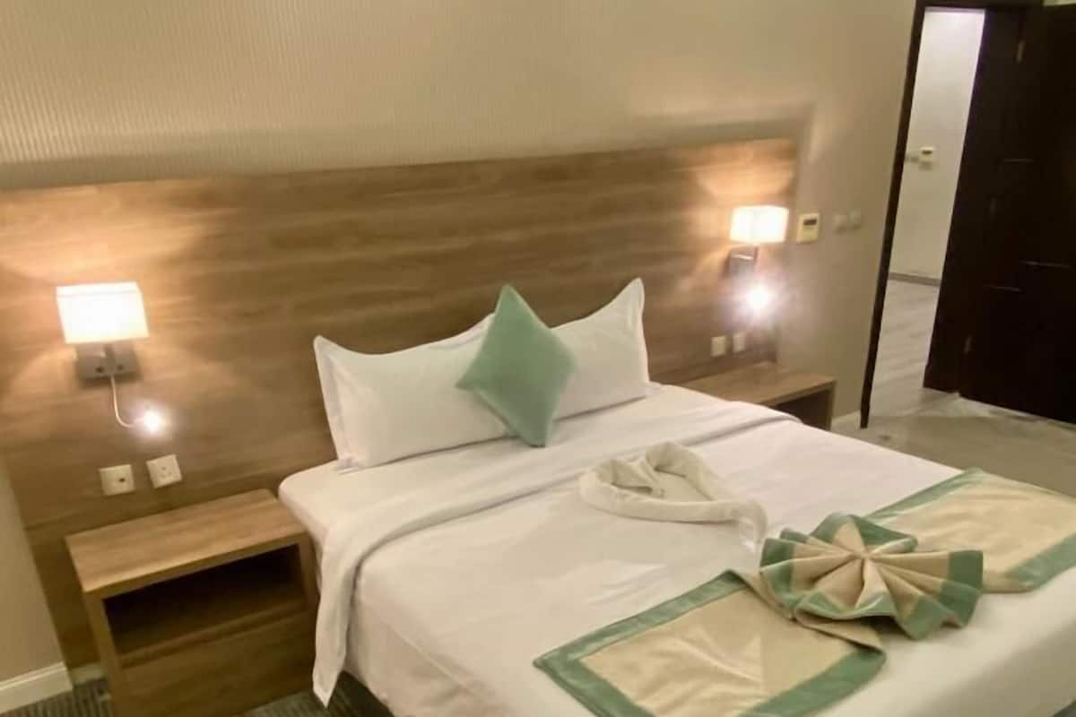 A neatly made bed with a green and white bedspread, two bedside lamps, and a wooden nightstand.