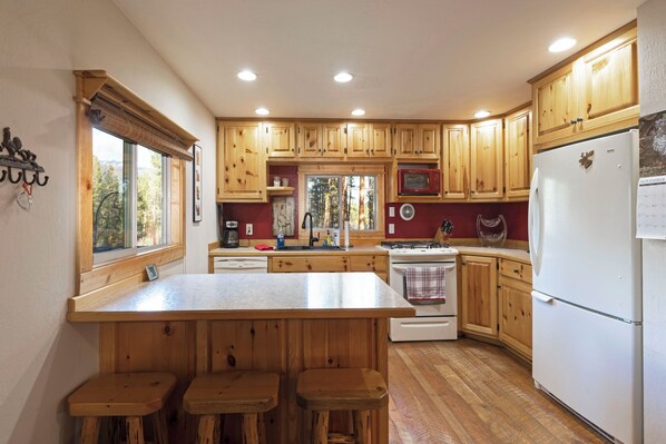 A kitchen with wooden cabinets, a central island with stools, a stove, and a refrigerator.