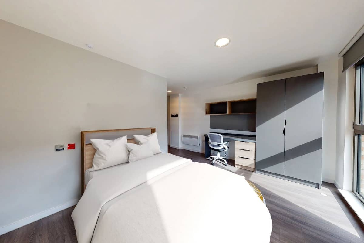 A modern hotel room with a large bed, a desk, and a wardrobe.