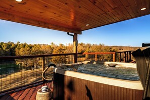 Een houten terras met een jacuzzi en uitzicht op bomen.