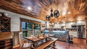 A spacious kitchen with wooden flooring, a dining area with a wooden table and benches, and a stone waterfall feature. - Private Pond, Weddings for up to 100! Pool is open (Sevierville)