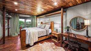 A bedroom with a wooden ceiling, a bed with a quilt, a desk with a chair, a mirror, and a window with curtains. - Private Pond, Weddings for up to 100! Pool is open (Sevierville)